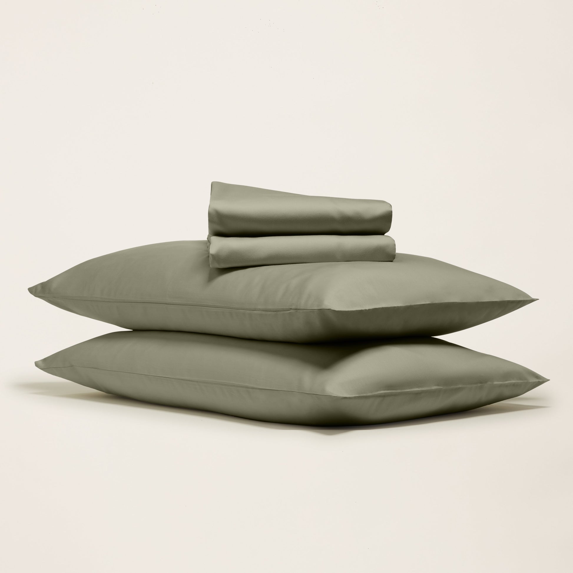 Set of green bedding including two pillows and a duvet cover on a light beige background