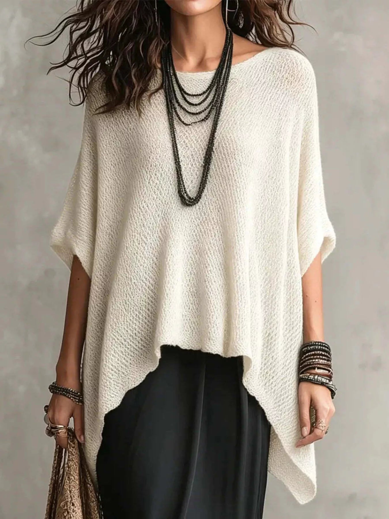 Woman wearing a white poncho over black pants with a neutral background