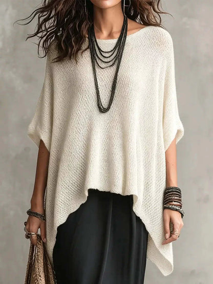 Woman wearing a white poncho over black pants with a neutral background