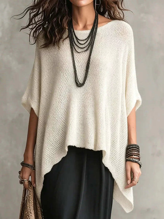 Woman wearing a white poncho over black pants with a neutral background