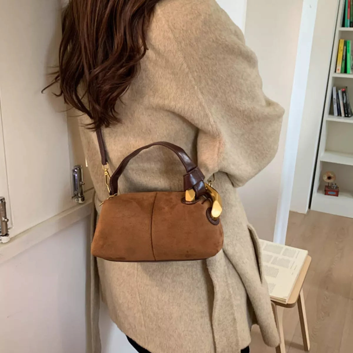 Person wearing a beige coat with a brown handbag indoors.
