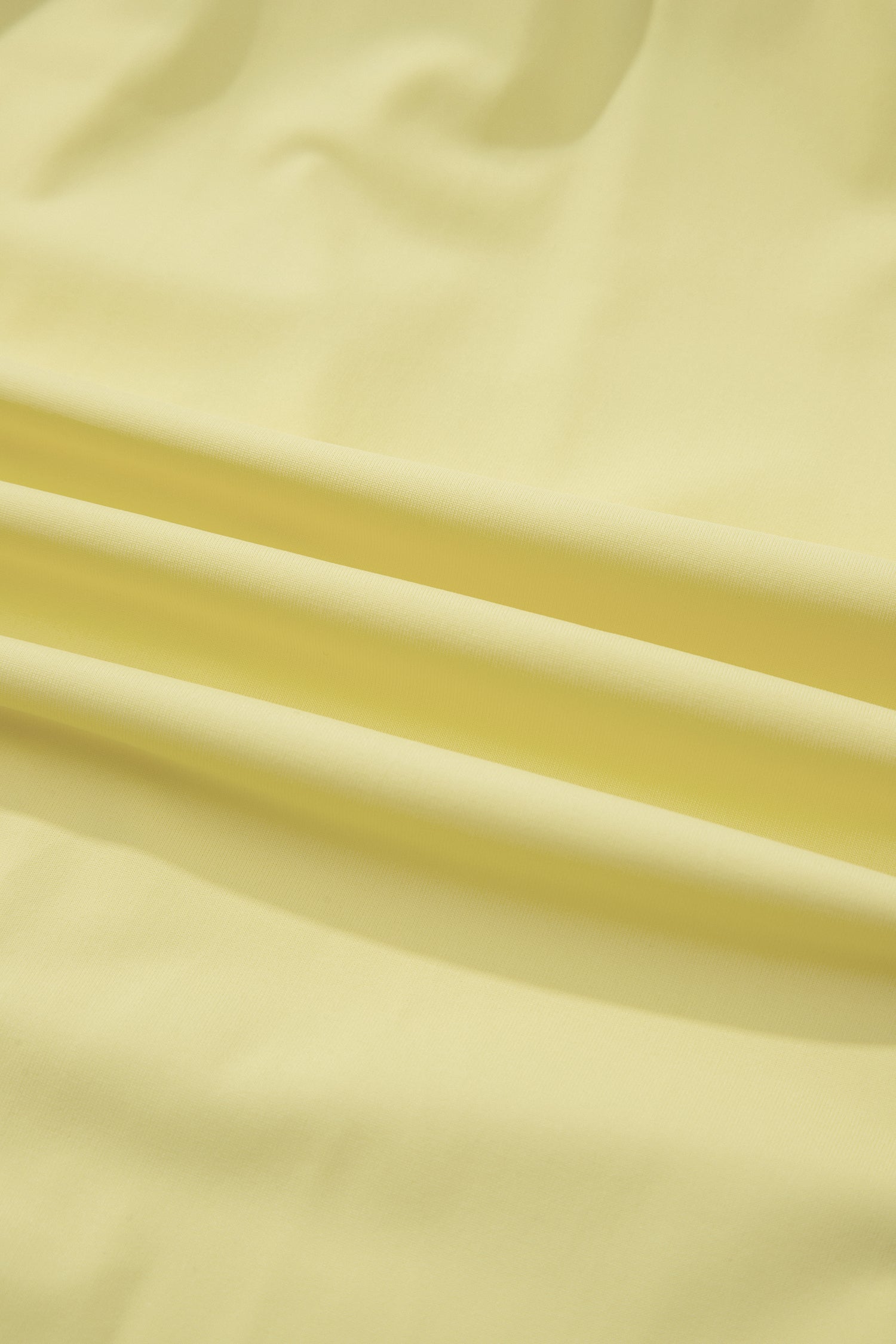 A close-up of pale pastel yellow fabric with soft folds and a smooth texture.