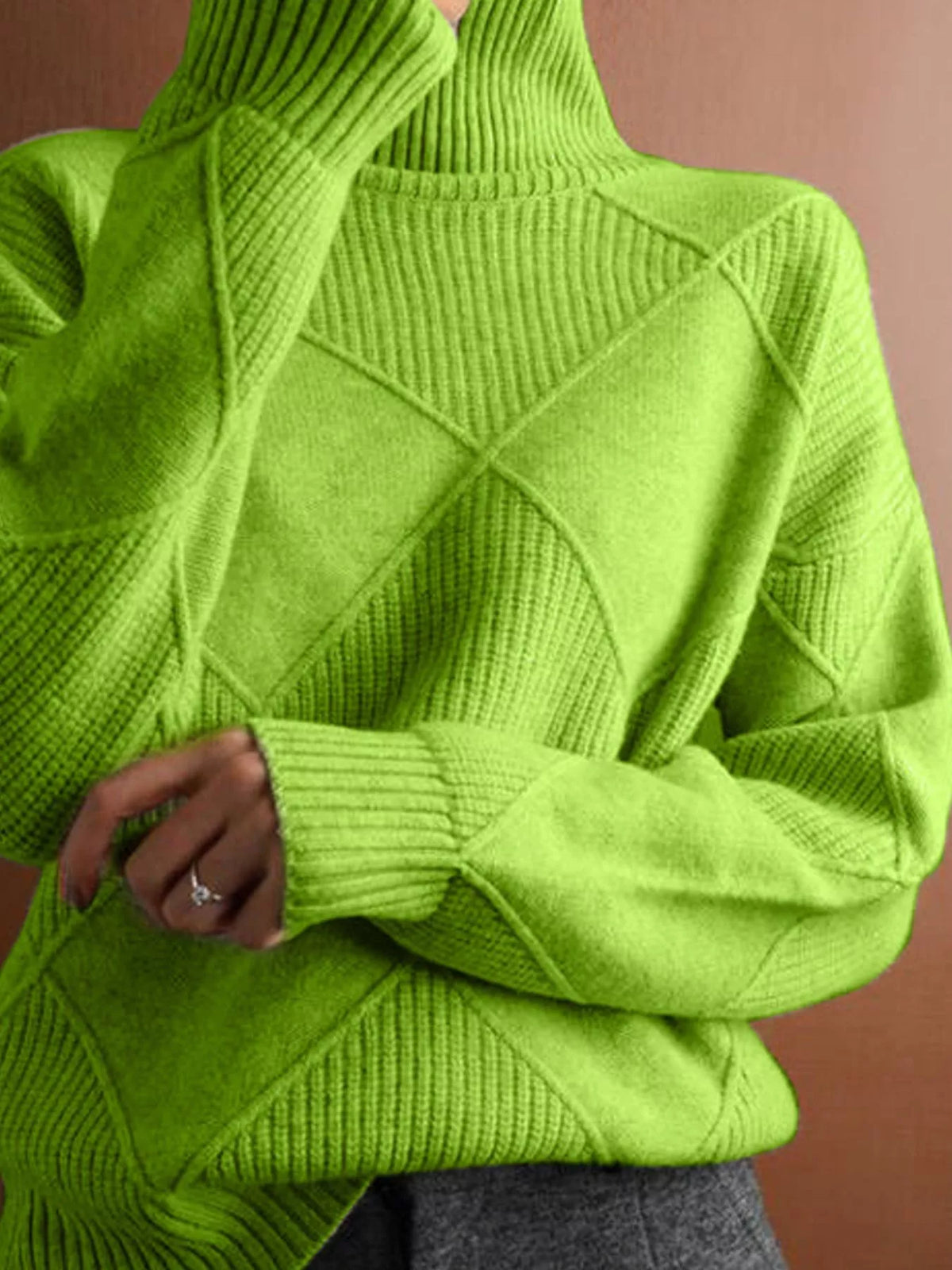 A close-up of a person wearing a bright lime green ribbed knit turtleneck sweater, showing the textured diamond-patterned chest and ribbed cuffs, with a hand resting near the hem.