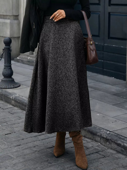 Person wearing a long dark gray skirt and brown boots on a city street.