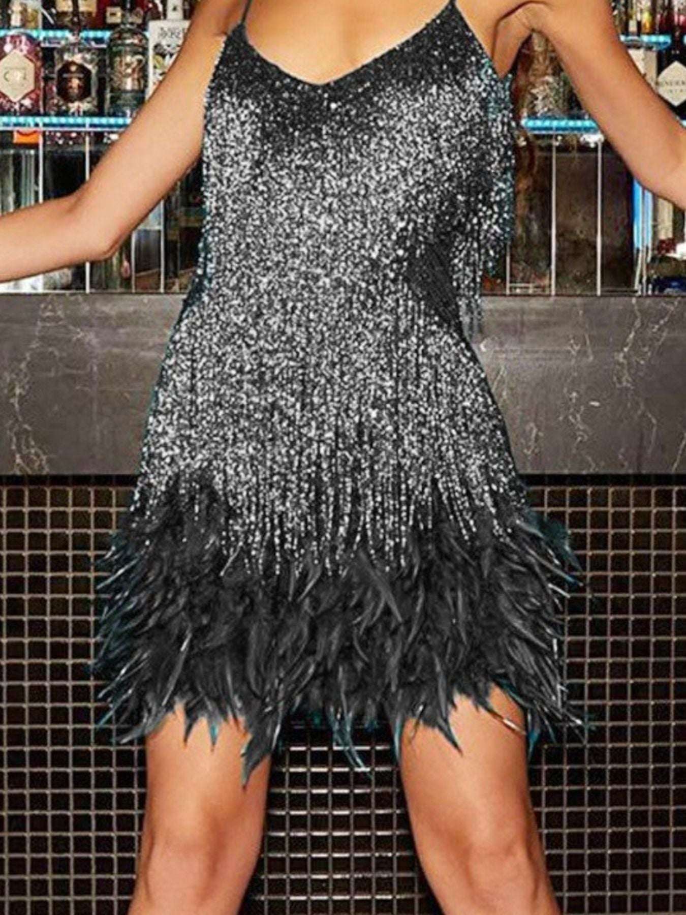 Person wearing a silver sequin and black feathered dress in front of a bar counter.
