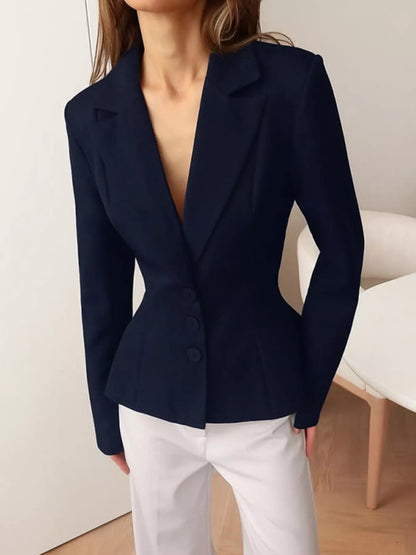 A woman wearing a fitted navy blue blazer with notch lapels and three front buttons, paired with white pants, shown in an indoor setting.