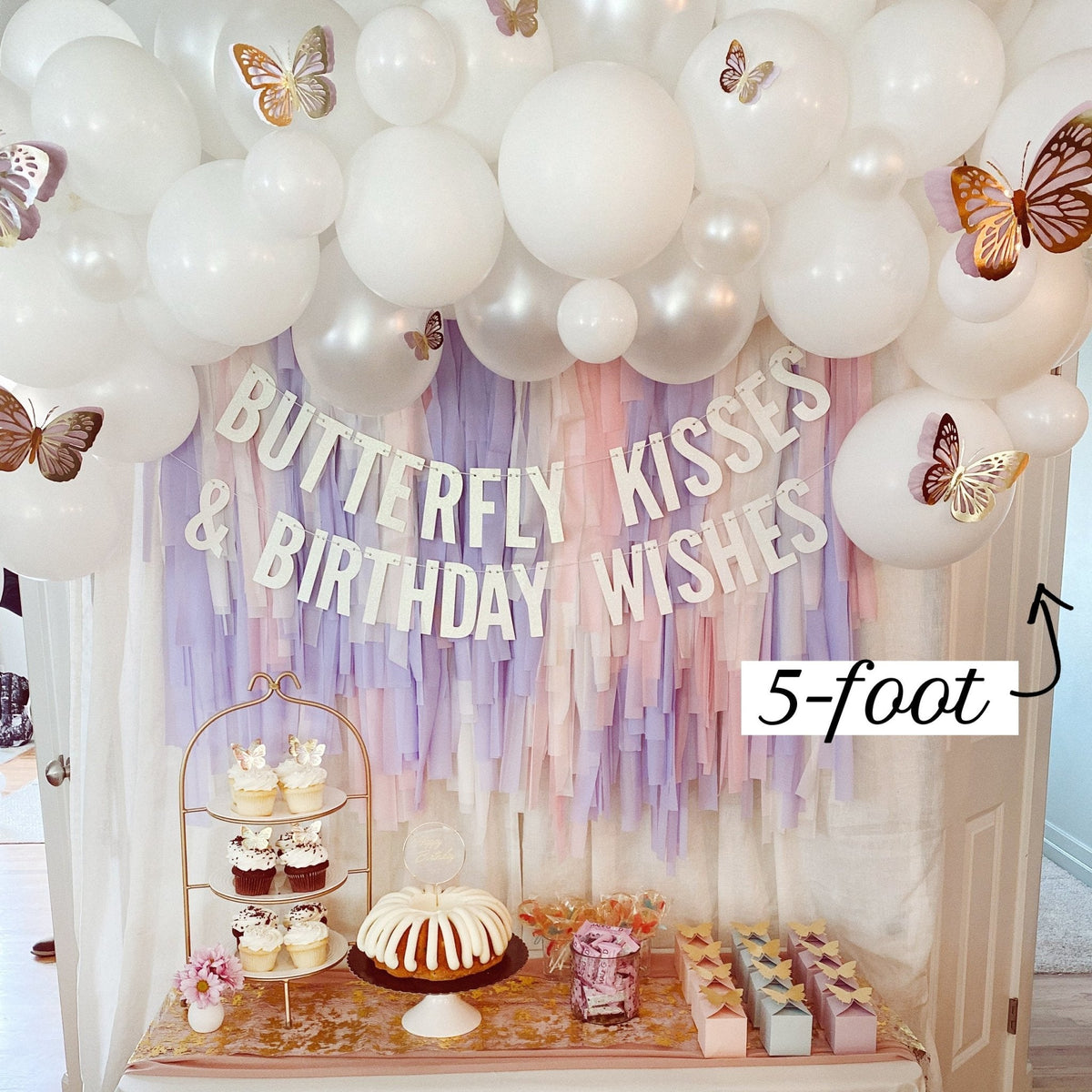 Decorative setup with balloons, a cake, and 'Butterfly Kisses & Birthday Wishes' banner.