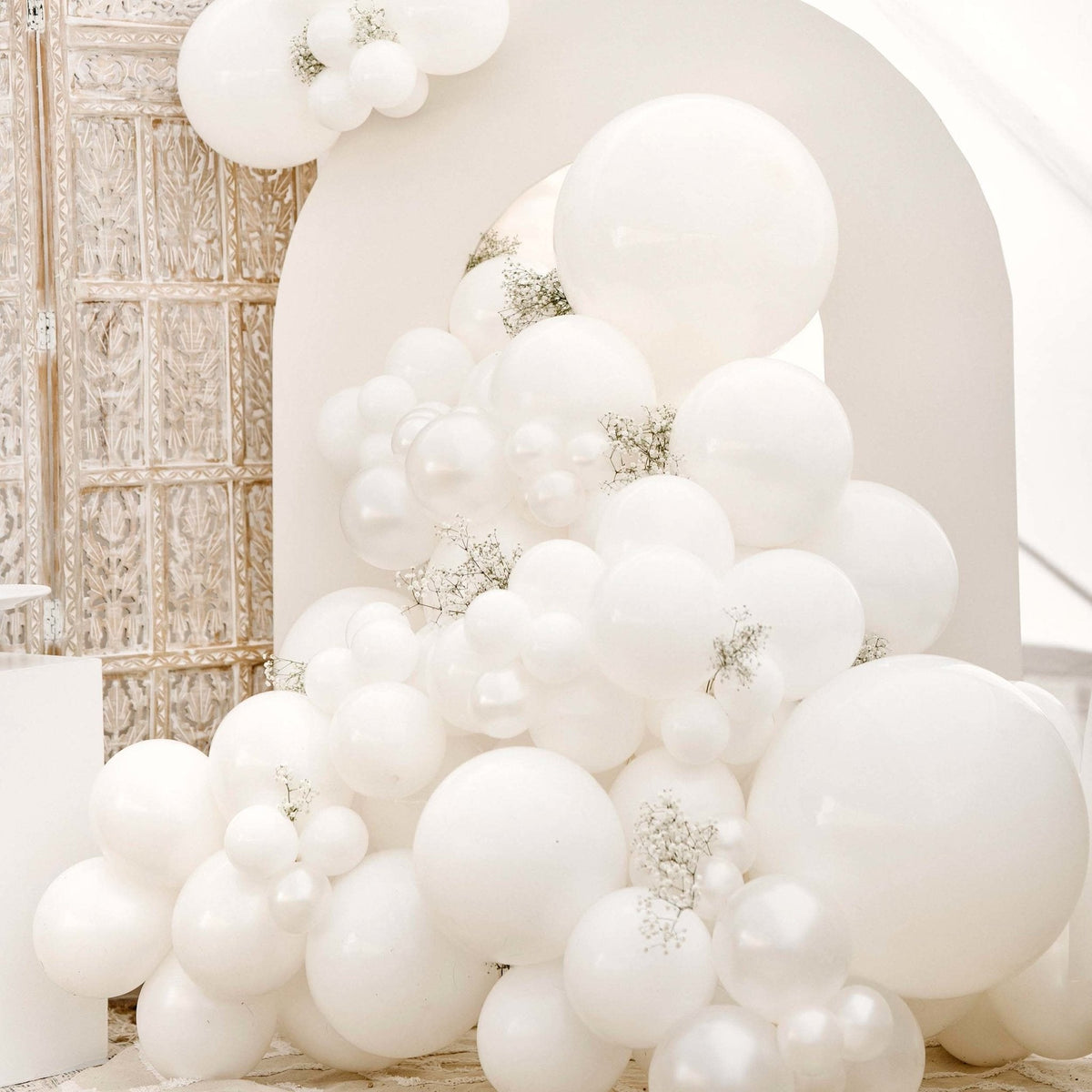 White balloon arch with decorative elements in a room setting