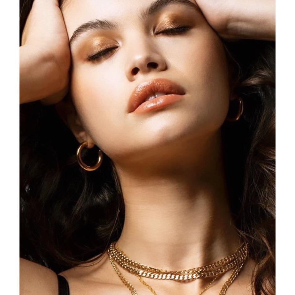 Close-up of a woman wearing gold jewelry with a neutral background
