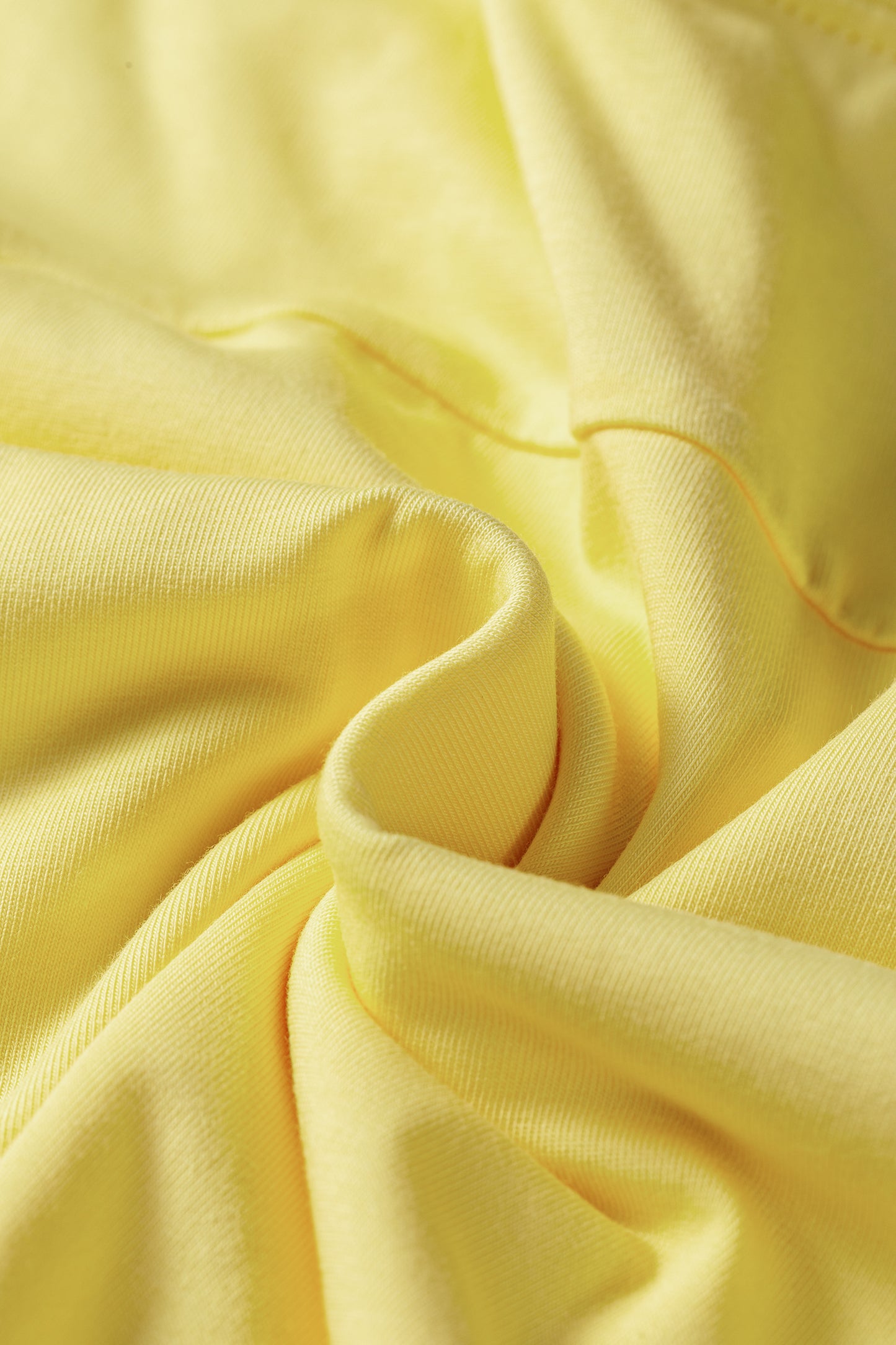 A close-up of draped light yellow fabric with soft folds and a smooth texture.