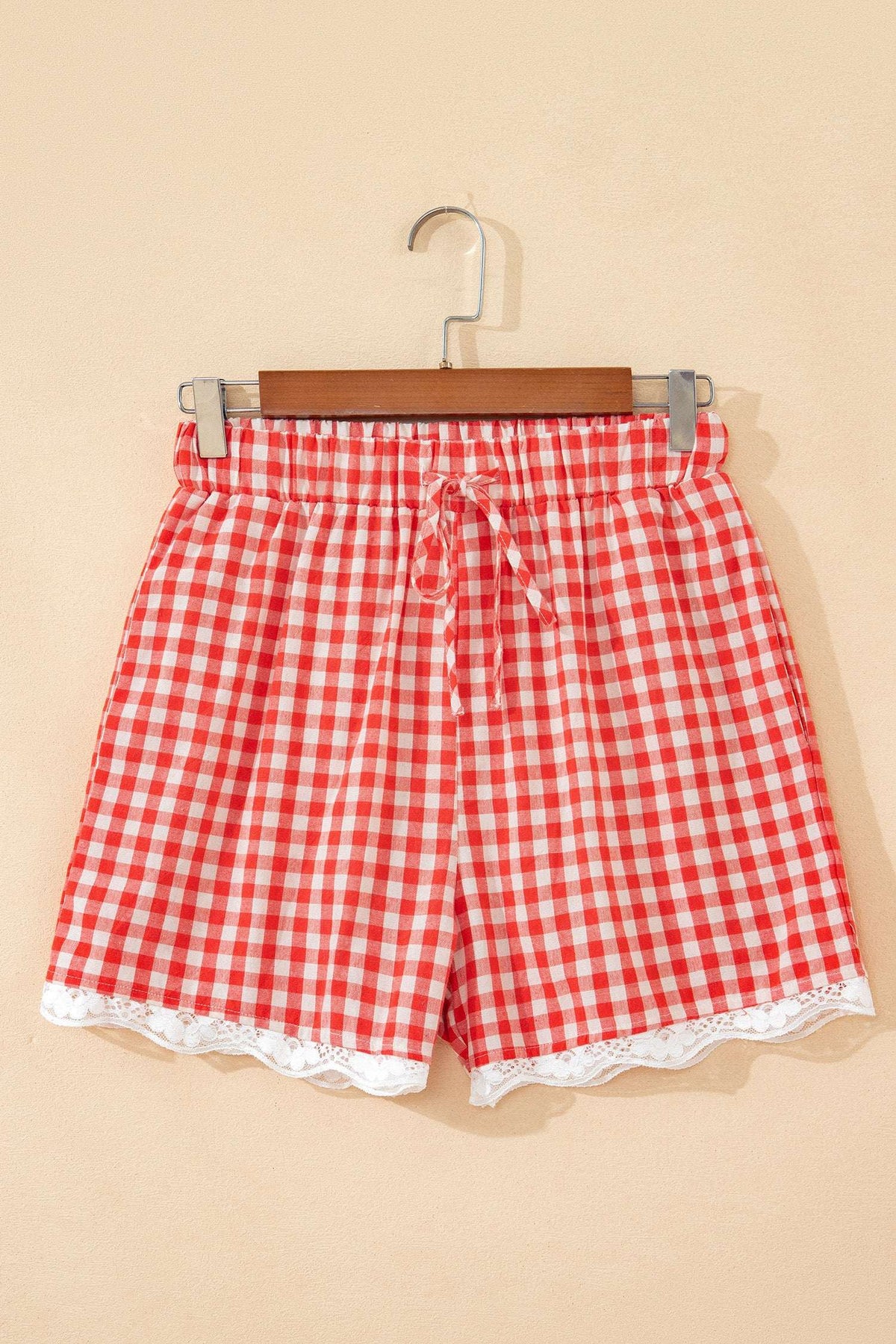 Red and white gingham fabric shorts with an elastic tie waist and white lace trim at the hem.
