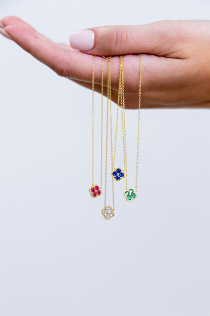 Three gold necklaces with floral pendants held in a hand against a white background