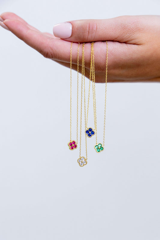 Three gold necklaces with floral pendants held in a hand against a white background