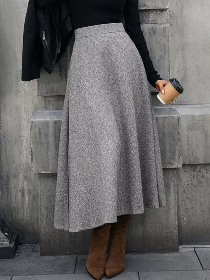 Person wearing a gray skirt and brown boots against a concrete wall.
