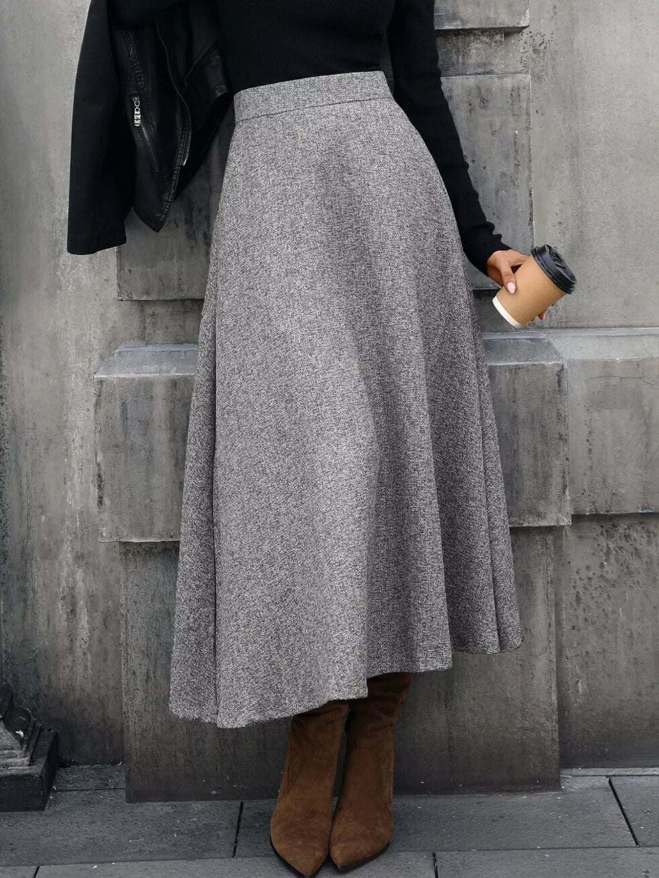 Person wearing a gray skirt and brown boots against a concrete wall.