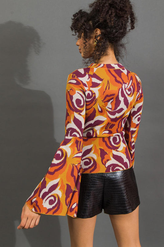 Person wearing a colorful patterned top and black shorts against a gray background