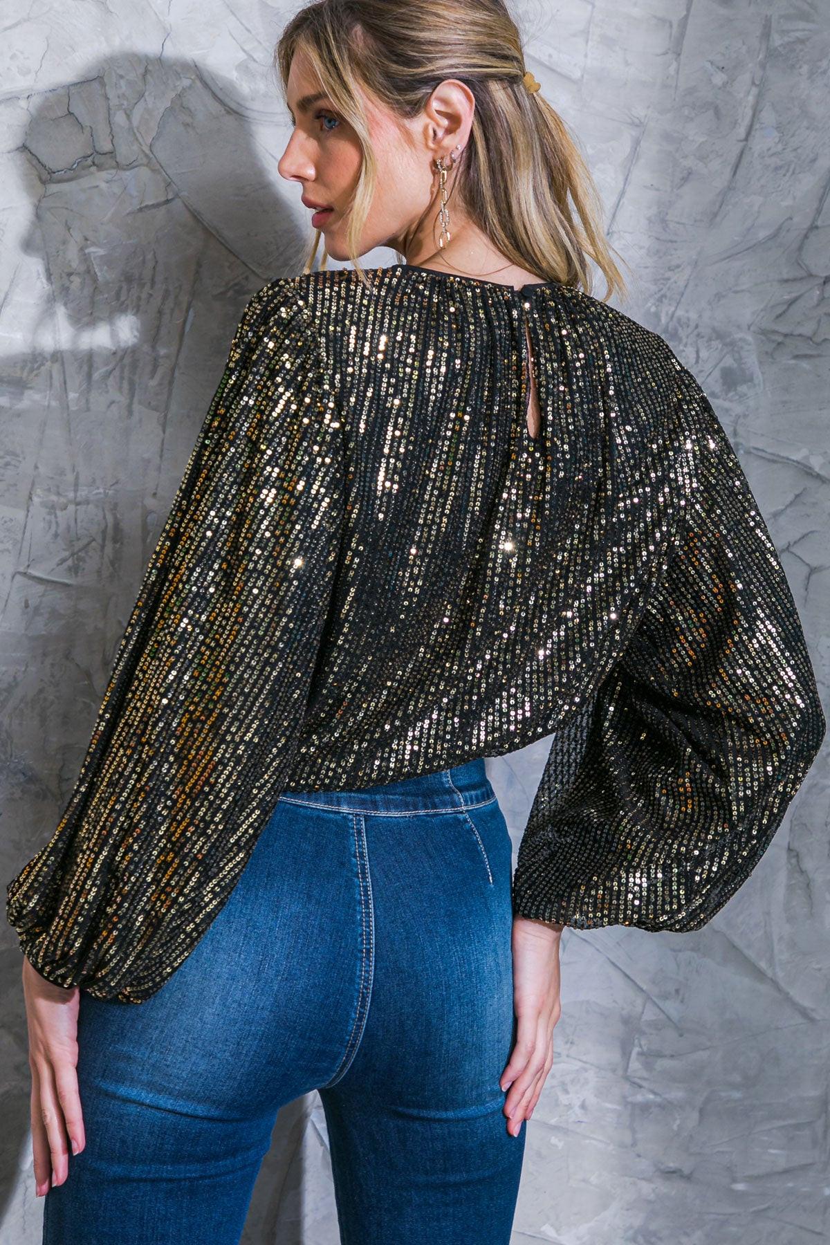 Woman wearing a black sequin top and blue jeans against a textured gray wall.
