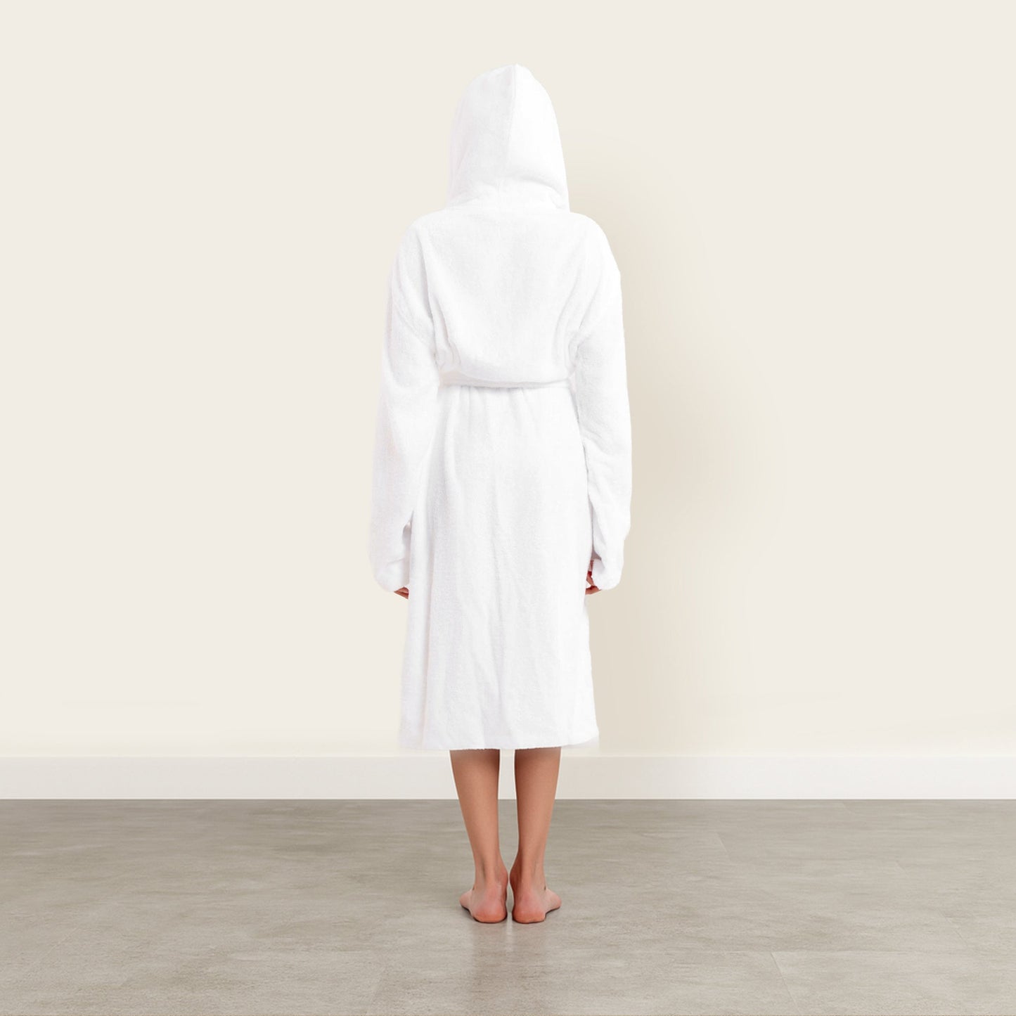 Person wearing a white robe standing in a minimalistic room with a light-colored wall and wooden floor.