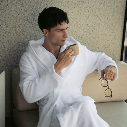 Man in a white robe holding a cup and glasses, sitting on a couch.