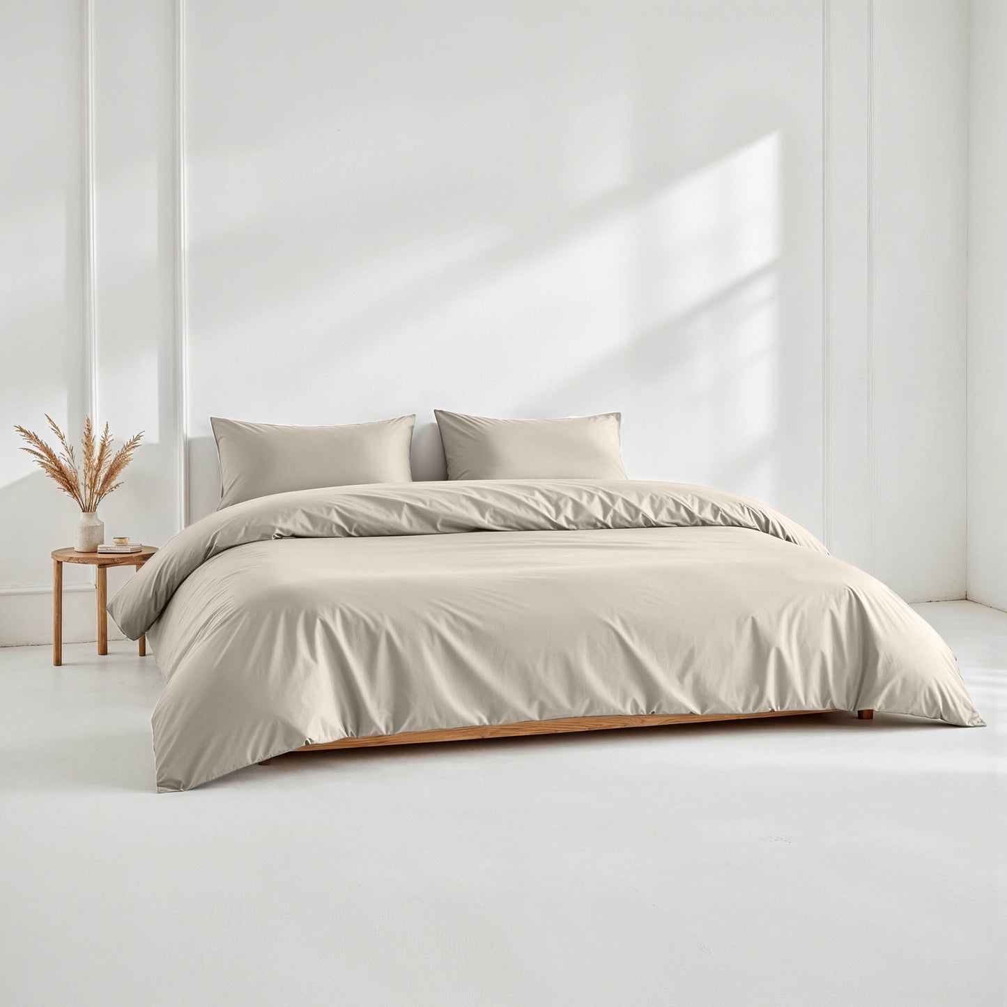Beige bedding set on a bed in a minimalistic room with a side table and plant.