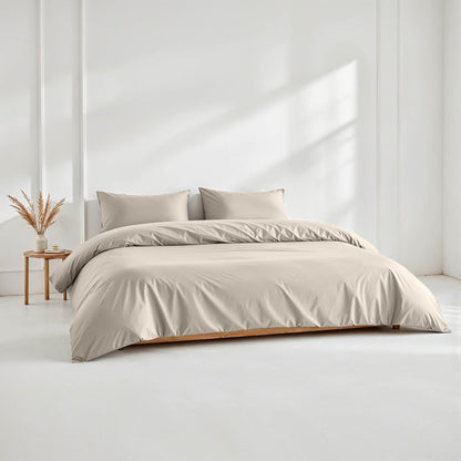 Beige bedding set on a bed in a minimalistic room with a side table and plant.