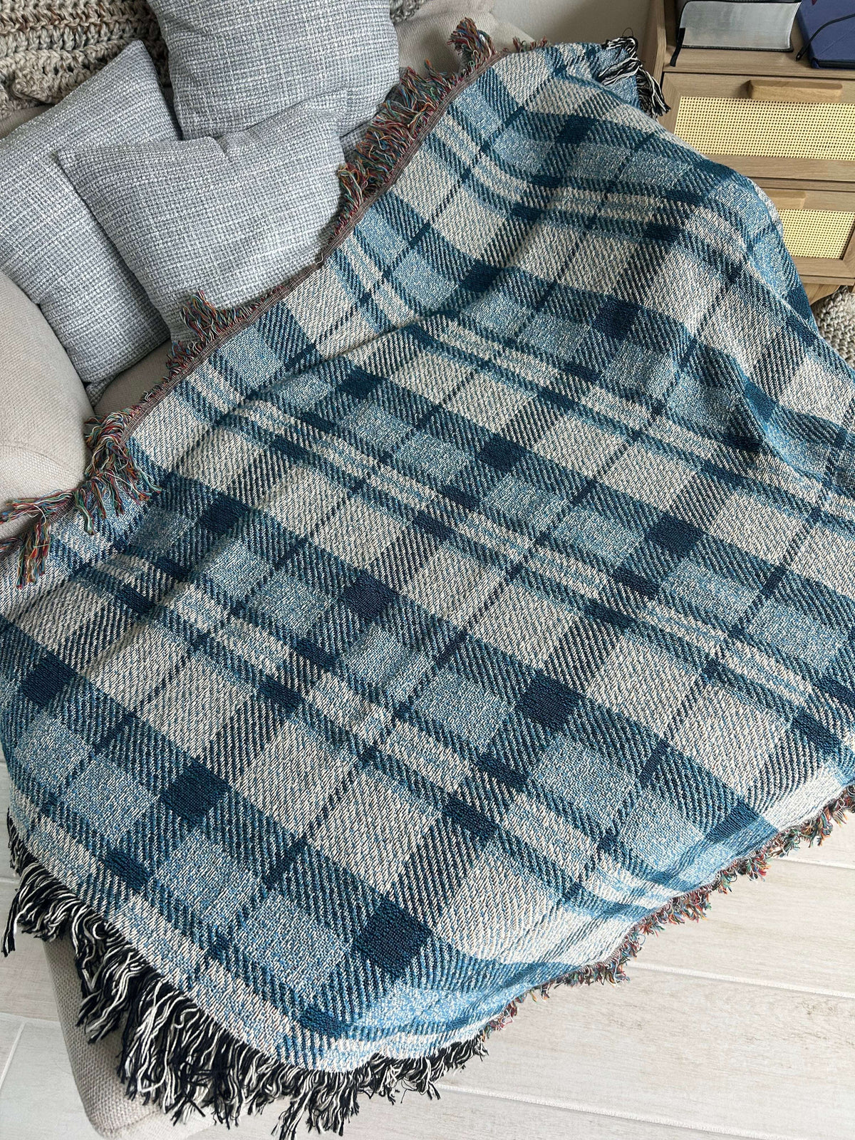 A blue and white plaid fringed throw blanket draped over a light gray upholstered chair in an indoor setting.
