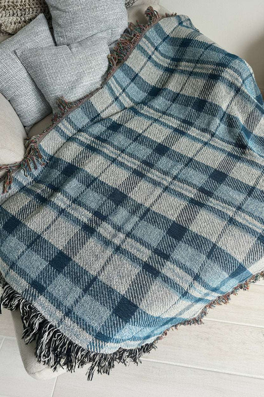 A blue and white plaid fringed throw blanket draped over a light gray upholstered chair in an indoor setting.