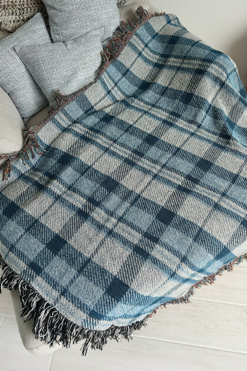 A blue and white plaid fringed throw blanket draped over a light gray upholstered chair in an indoor setting.