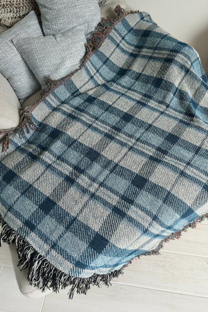 A blue and white plaid fringed throw blanket draped over a light gray upholstered chair in an indoor setting.