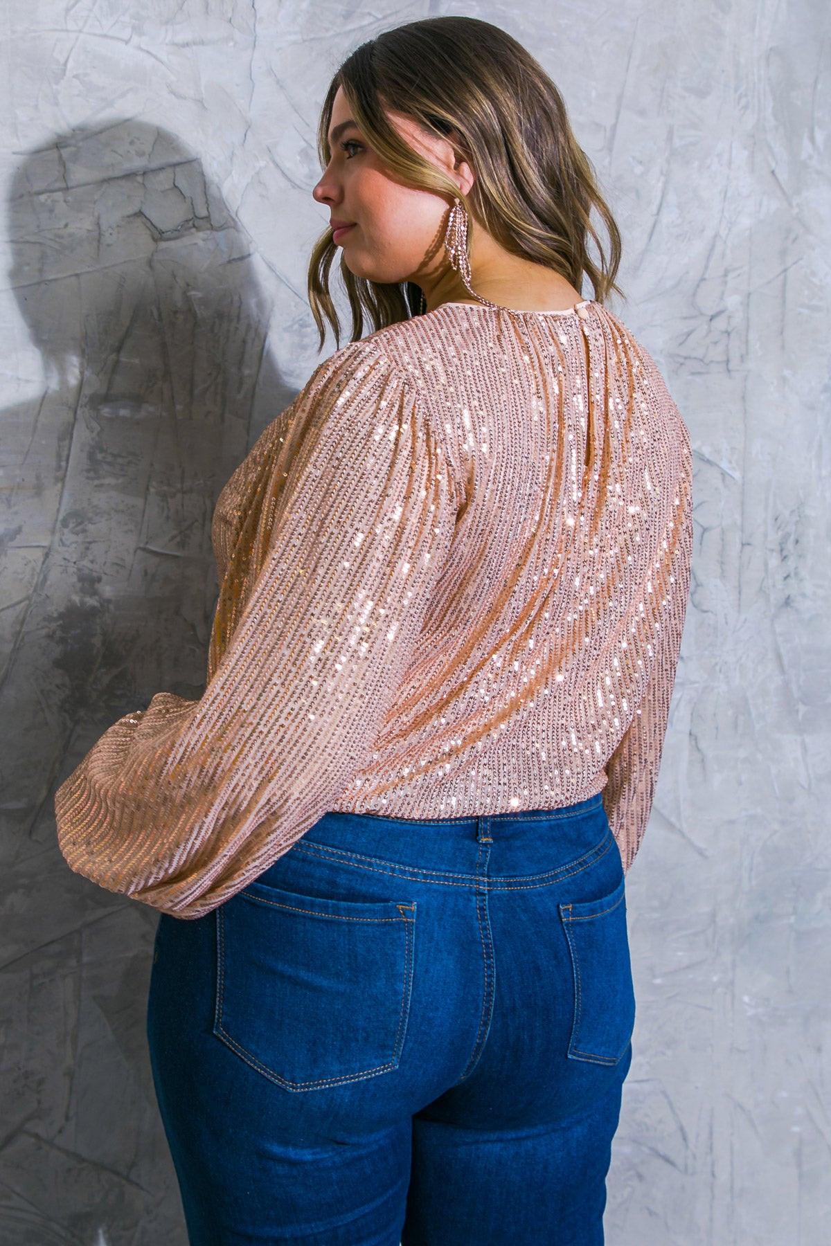 Woman wearing a sparkly top and blue jeans against a textured gray wall.