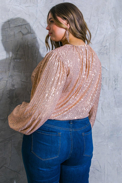 Woman wearing a sparkly top and blue jeans against a textured gray wall.