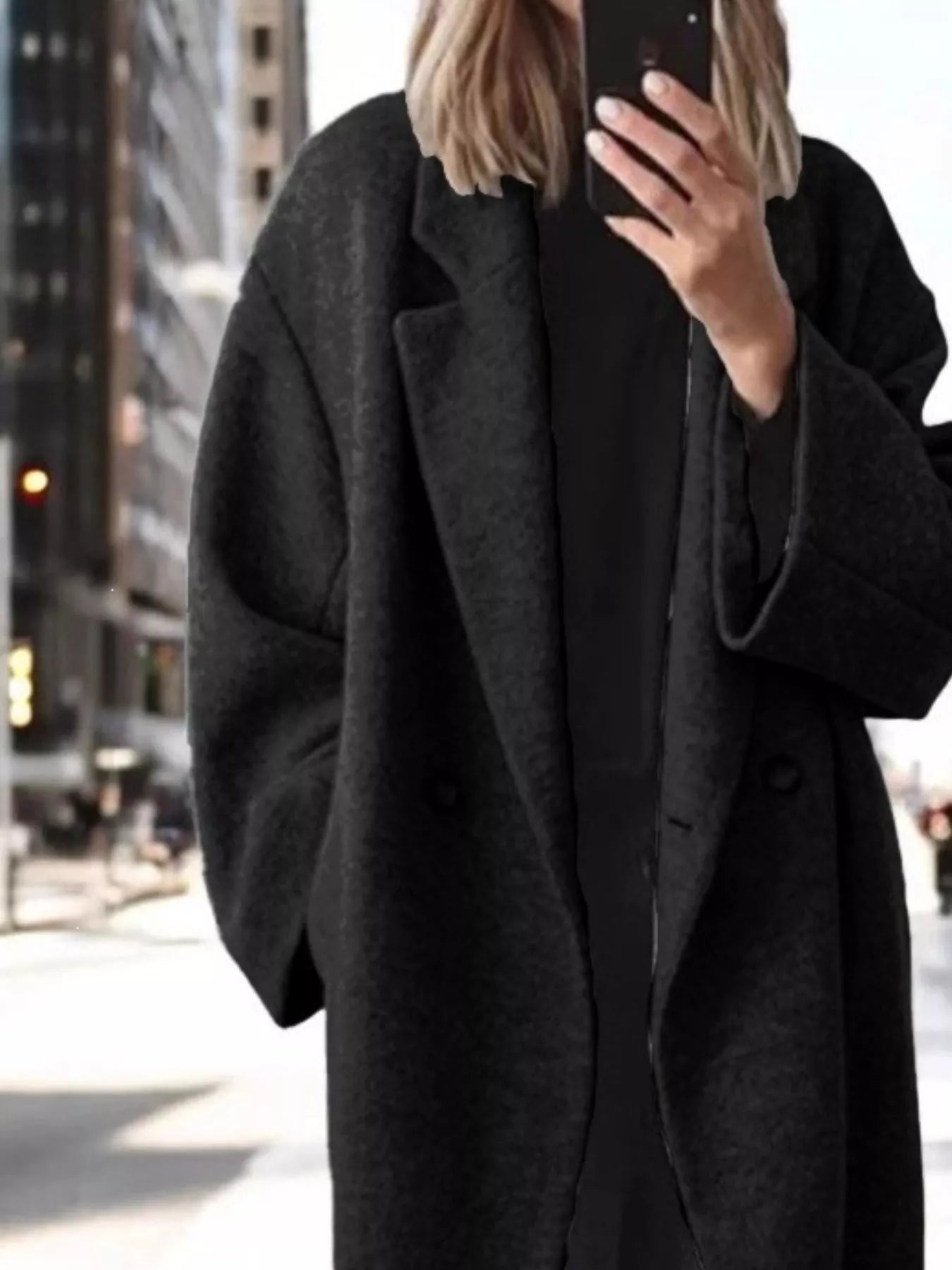 A person taking a mirror selfie in an urban setting, wearing an oversized dark charcoal gray wool-blend coat over a black outfit.