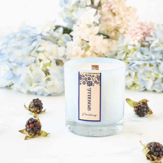 Blackberry Private Reserve candle in a clear glass jar, surrounded by blackberries and light blue flowers.