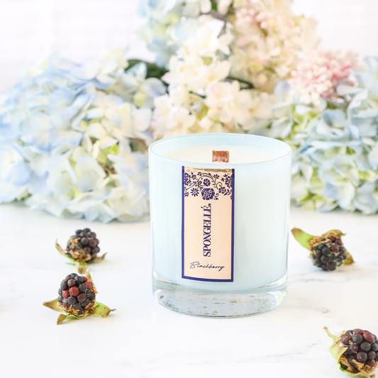 Blackberry Private Reserve candle in a clear glass jar, surrounded by blackberries and light blue flowers.