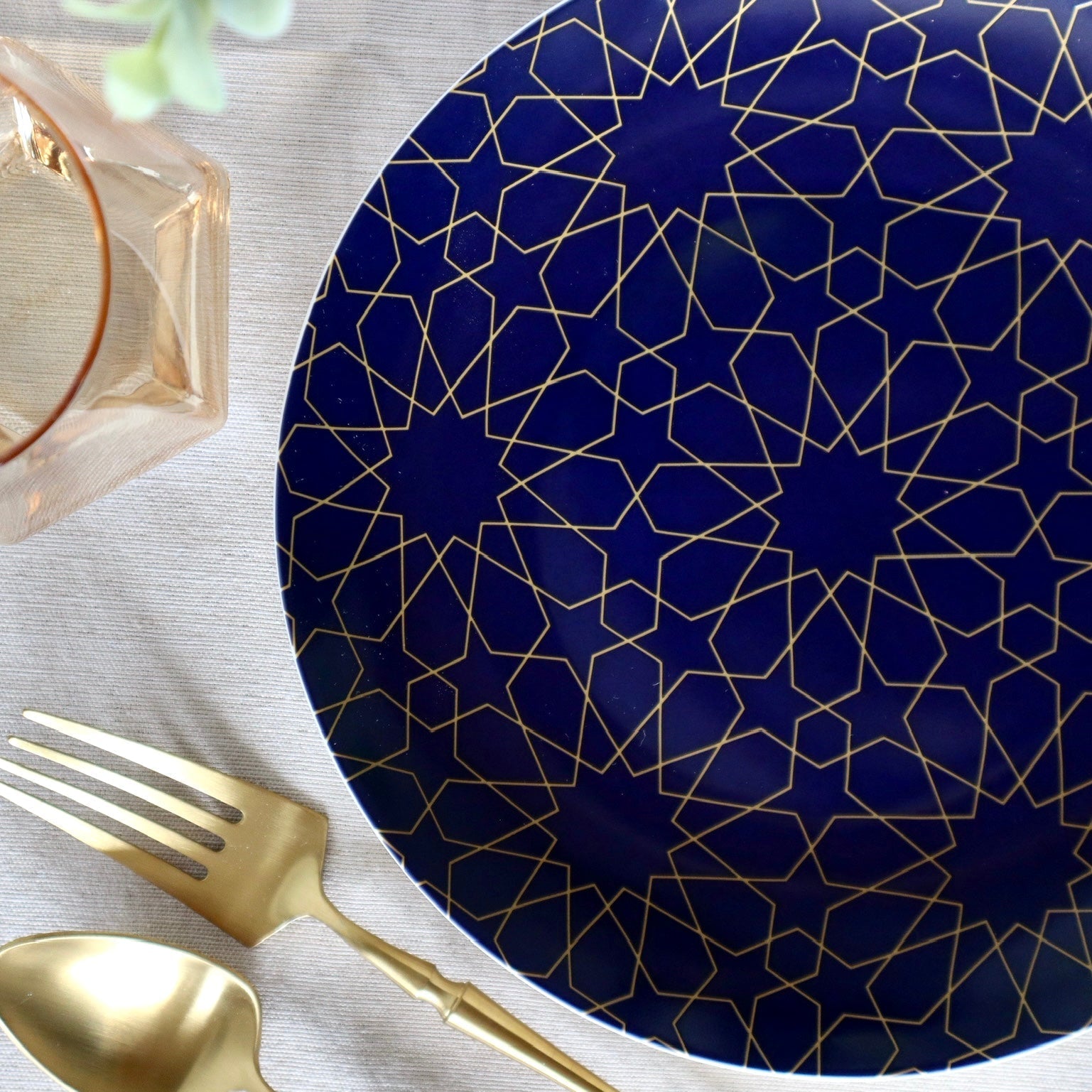 Navy blue plate with gold geometric pattern on a white surface with gold fork and spoon.