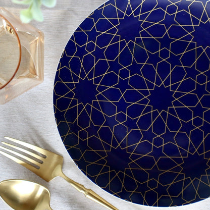 Navy blue plate with gold geometric pattern on a white surface with gold fork and spoon.