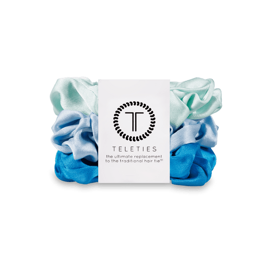 Two light blue and one blue scrunchie on a black stand with a Teleties branded card in the center.