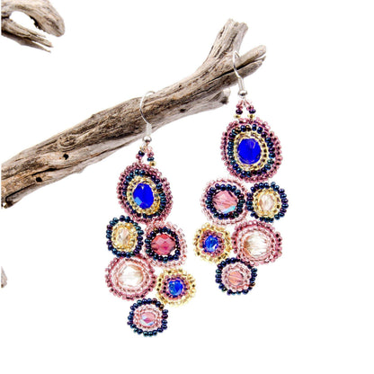 Colorful beaded earrings on a white background with a piece of driftwood.