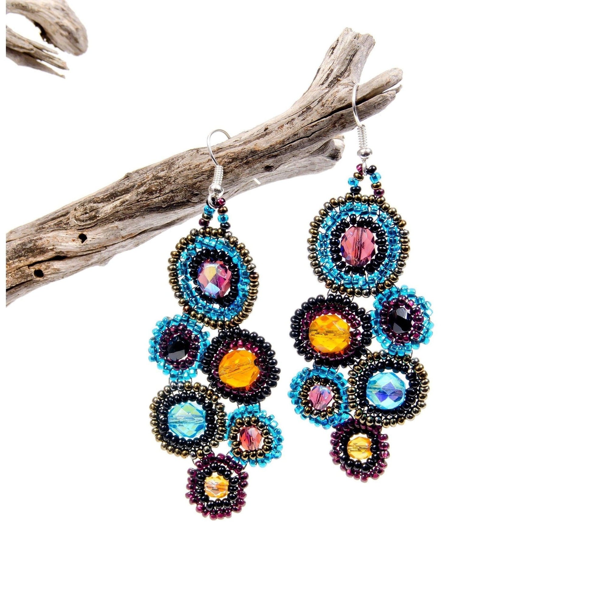 Colorful beaded earrings hanging from a branch on a white background