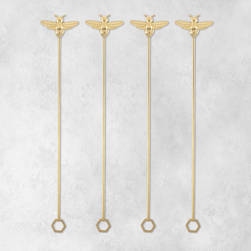 Four gold bumble bee stir sticks arranged side by side on a light gray background.