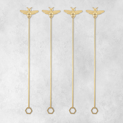 Four gold bumble bee stir sticks arranged side by side on a light gray background.