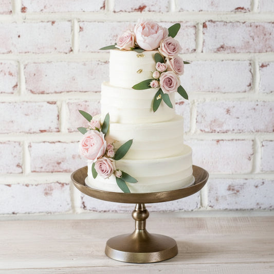 Bronze cake stand with a wedding cake on a light wooden surface and white brick wall background