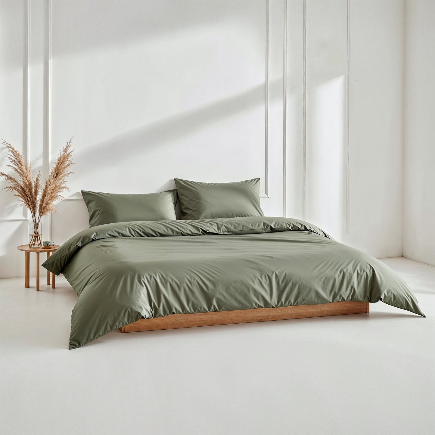 Green bedding set on a bed in a minimalistic room with a side table and decorative plant.