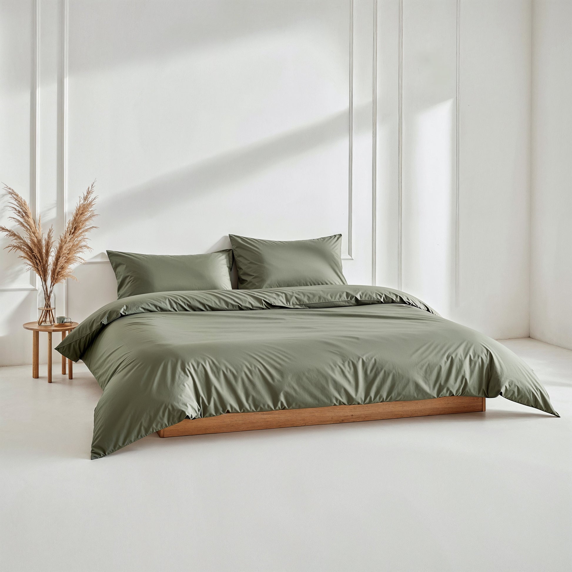 Green bedding set on a bed in a minimalistic room with a side table and decorative plant.
