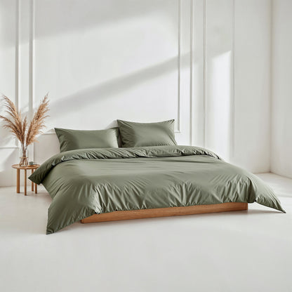 Green bedding set on a bed in a minimalistic room with a side table and decorative plant.