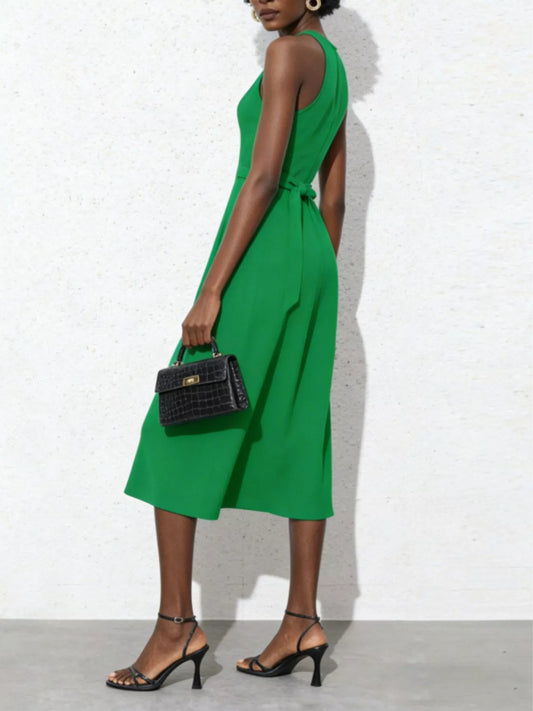 Woman wearing a green dress holding a black handbag against a white background