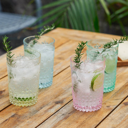 Four glasses of iced beverages with garnishes on a wooden table outdoors.
