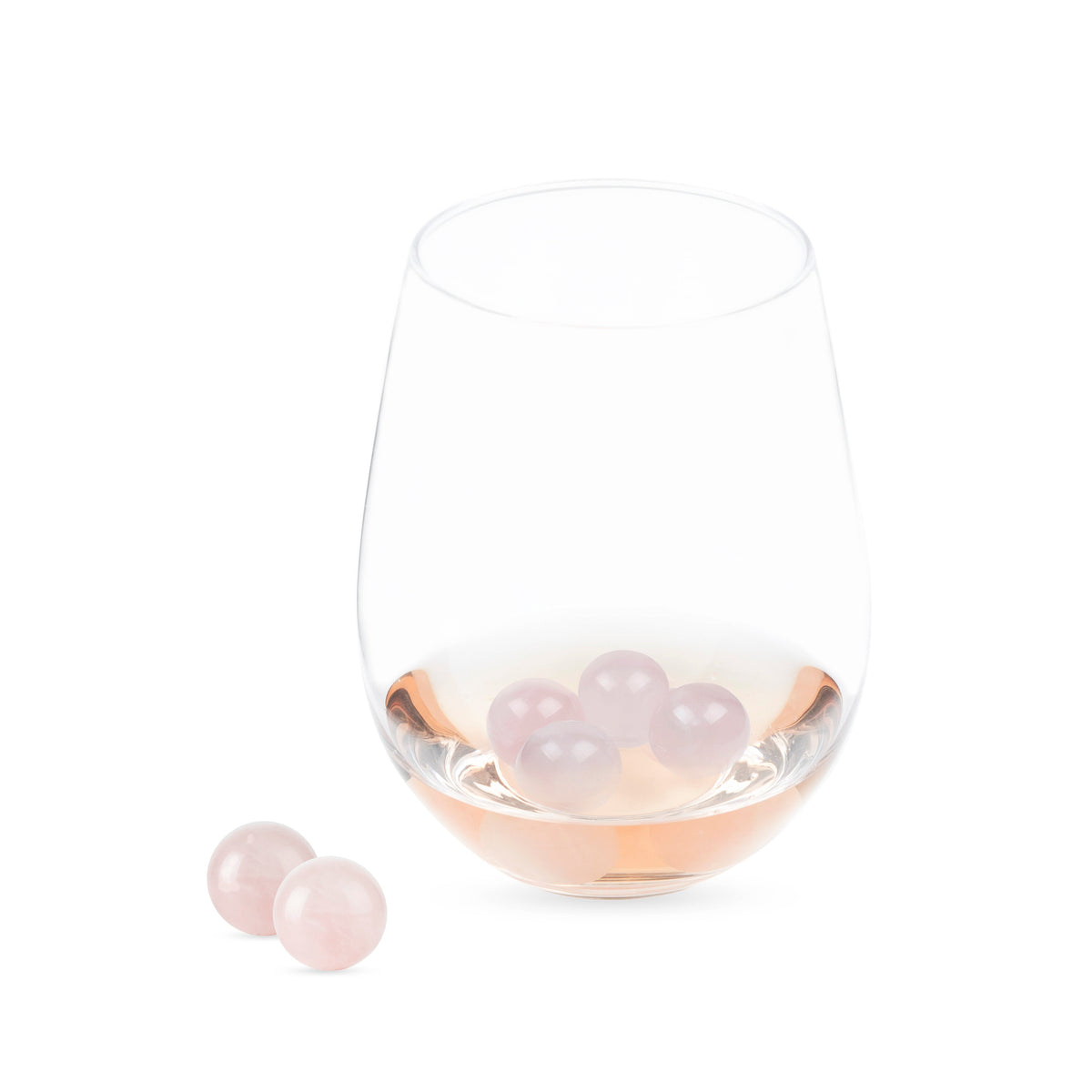 Rose quartz wine gems inside a stemless wine glass, with two pink stones beside it.