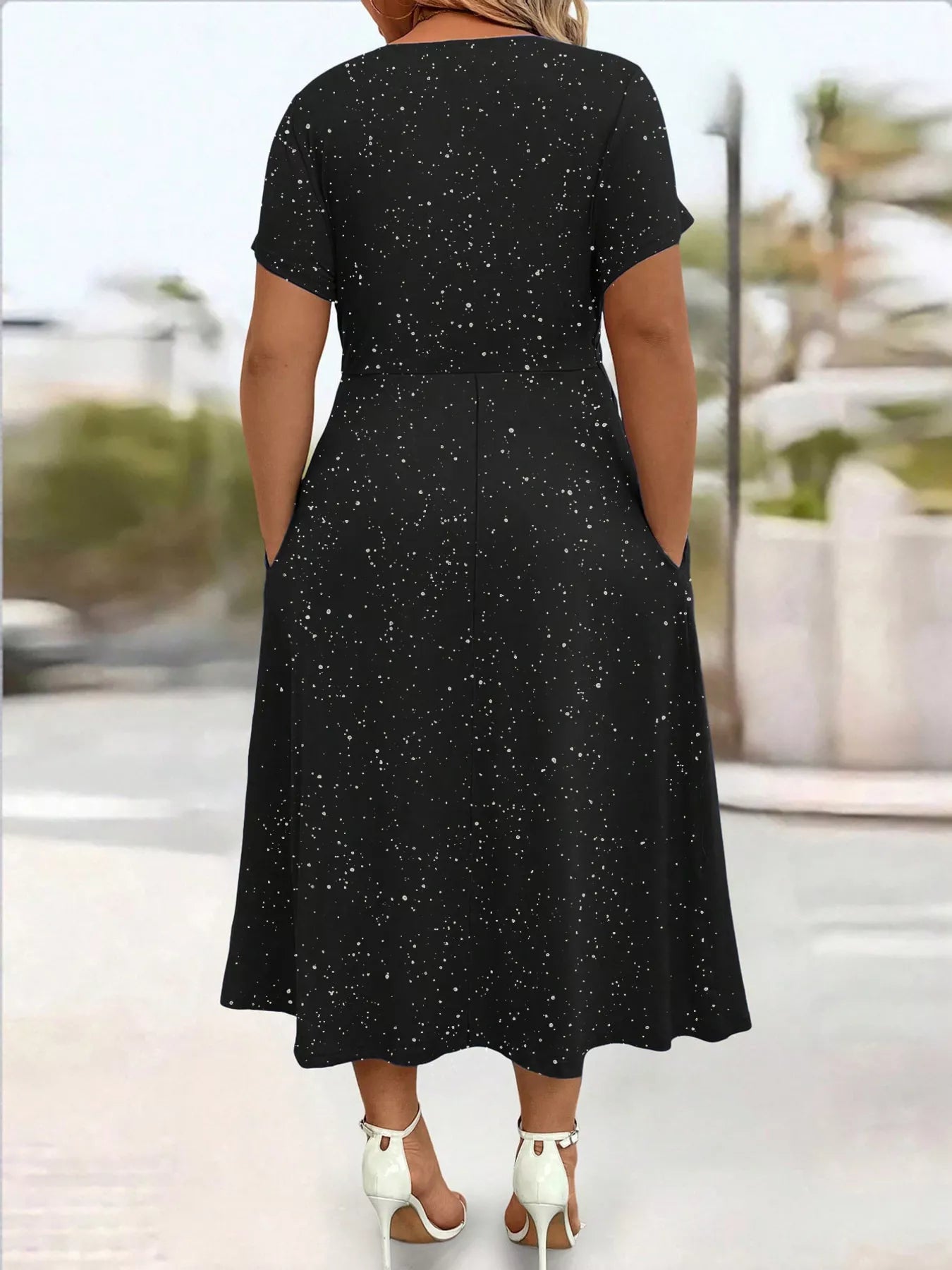 Black dress with white speckles worn by a person, blurred outdoor background