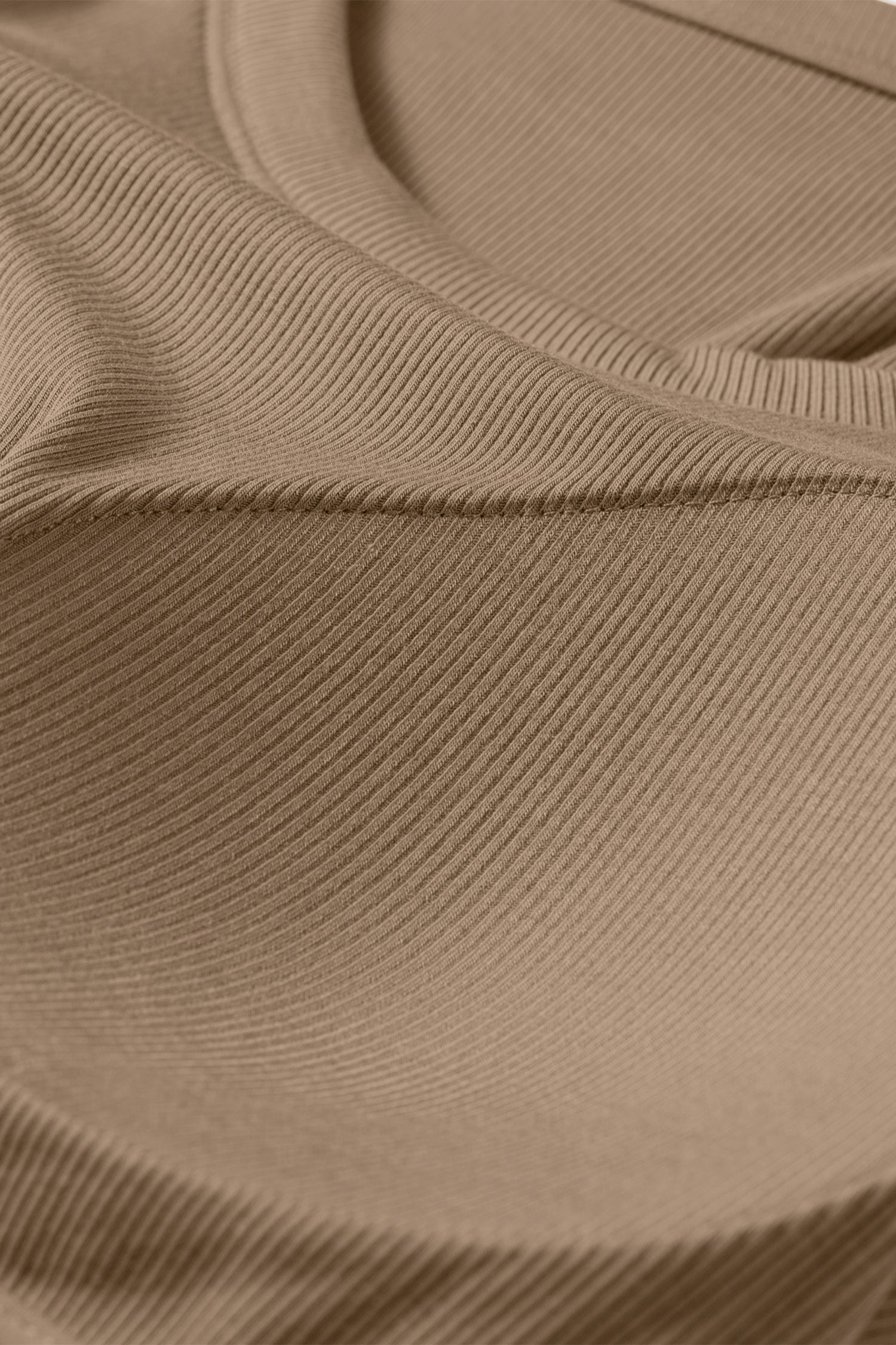 Close-up of a tan ribbed fabric tank top showing the textured material and curved seam of a padded bust.